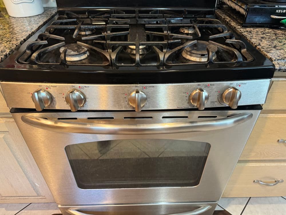 Stainless steel gas stove with multiple burners and oven, set on a granite countertop.